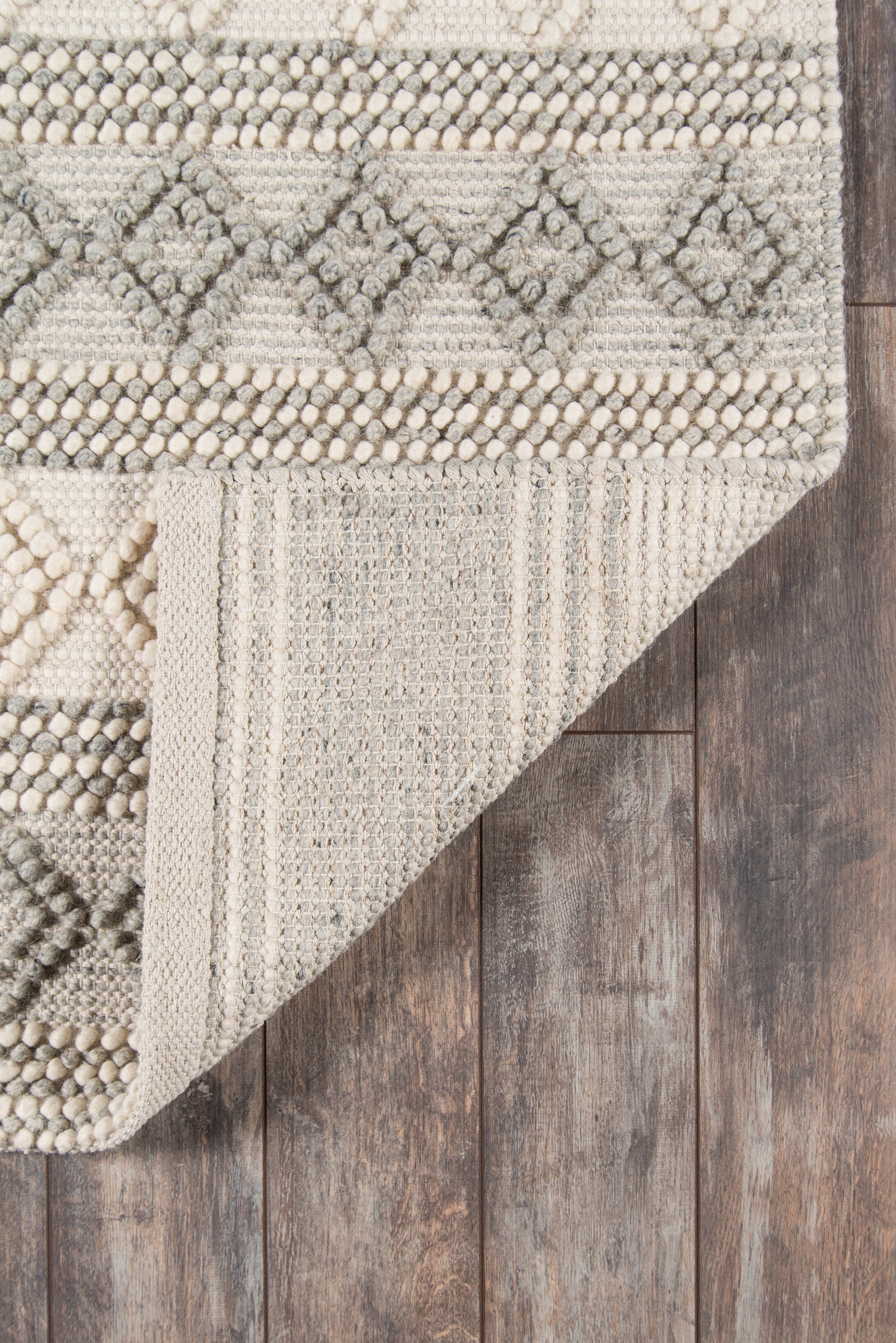 Ivory and taupe geometric rug with diamond and pebble textures, woven boho style on dark wood floor.