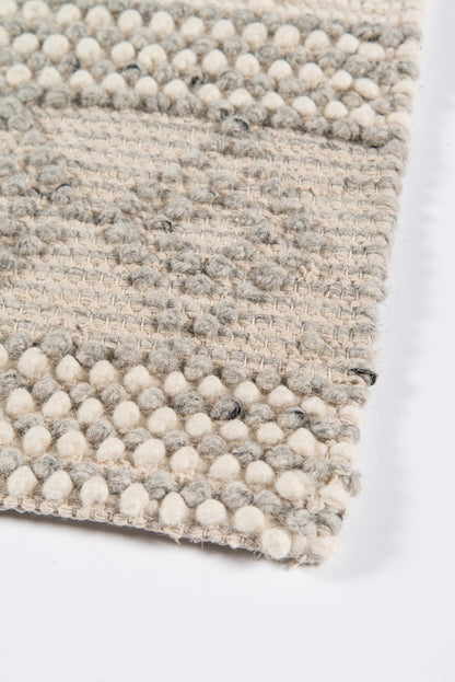 Ivory-beige woven rug with pompom edge trim and textured striped surface.