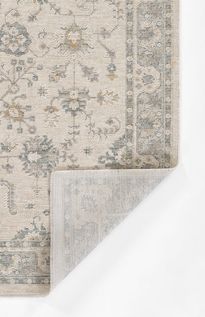 Light blue-gray oriental rug with ivory floral motifs and ornate border; folded corner reveals backing.