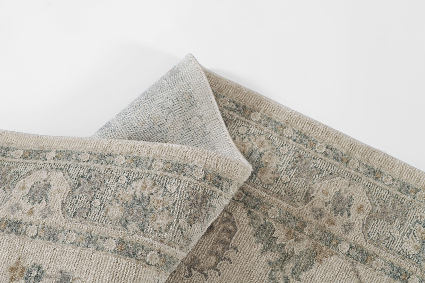Rectangular woven rug in muted blue and beige with distressed floral medallion pattern; folded corner.