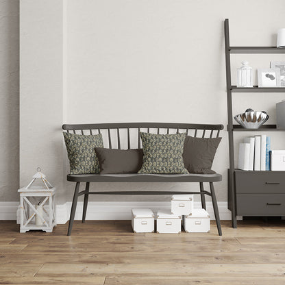 Dark metal bench with gray cushion, two green patterned pillows; white boxes beneath, lantern left, tall shelving unit right.