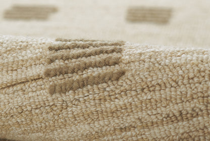 Beige woven rug close-up with tight loop pile and folded edge, natural wool texture.