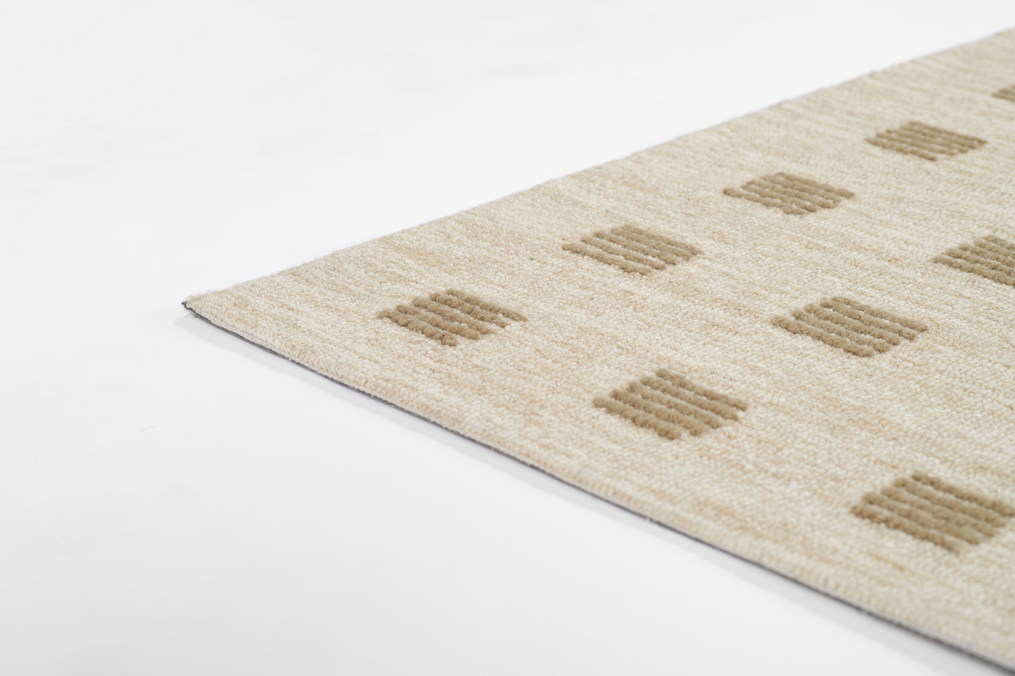 Beige textured rug with tan square block motifs; diagonal corner visible.