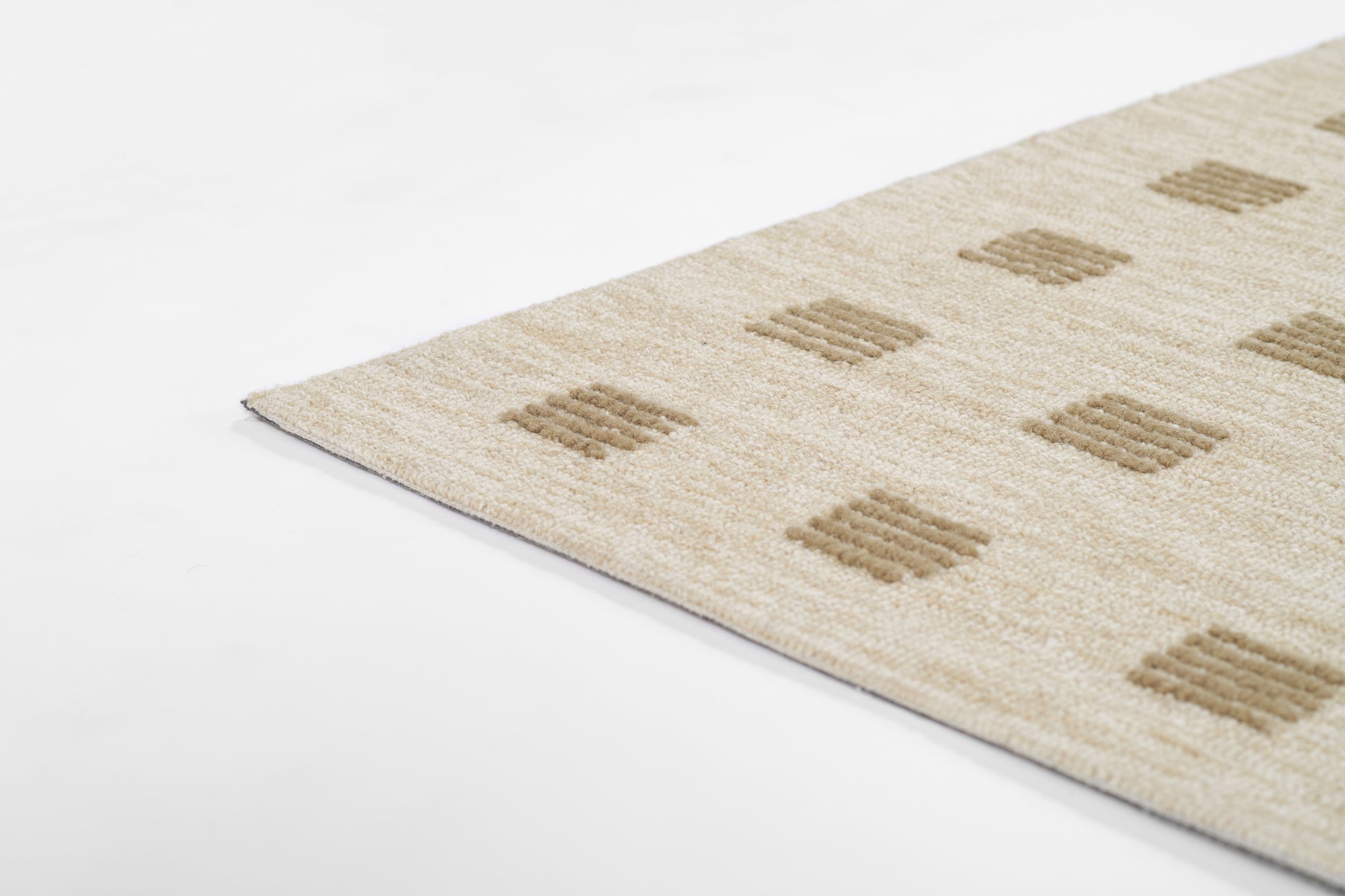 Beige textured rug with tan square block motifs; diagonal corner visible.