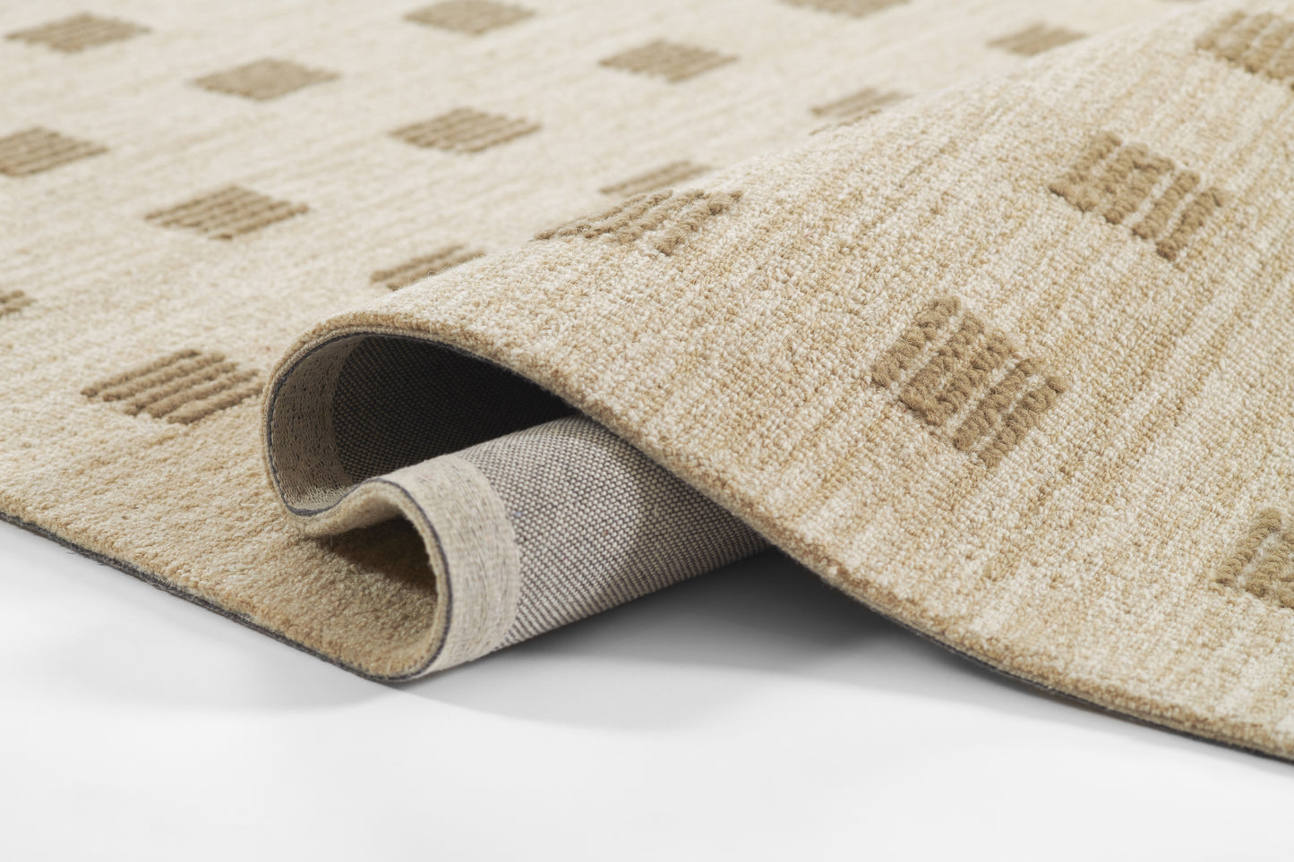 Beige woven area rug with light brown diamond pattern; rolled edge reveals gray backing & soft pile.