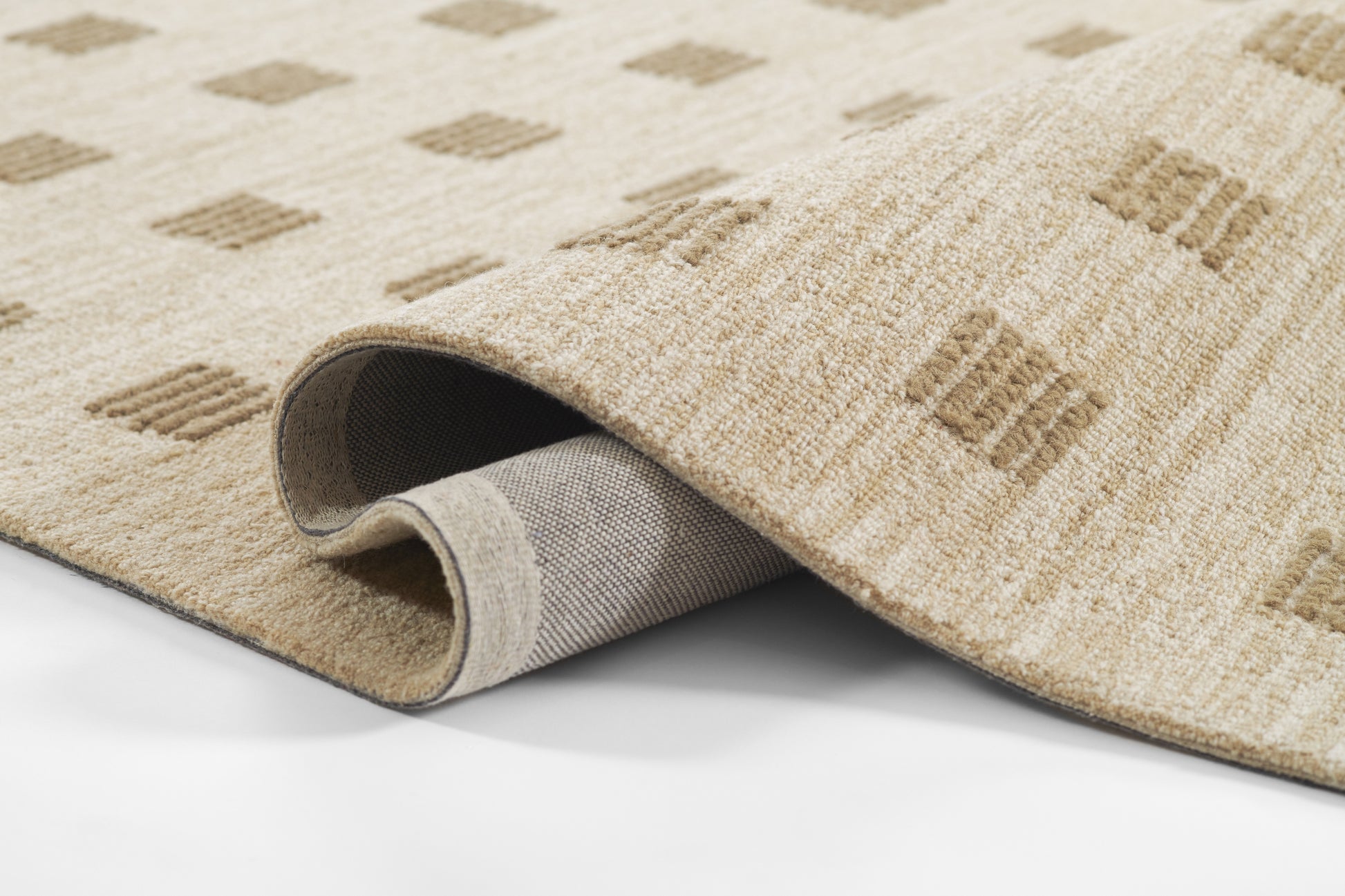 Beige woven area rug with light brown diamond pattern; rolled edge reveals gray backing & soft pile.