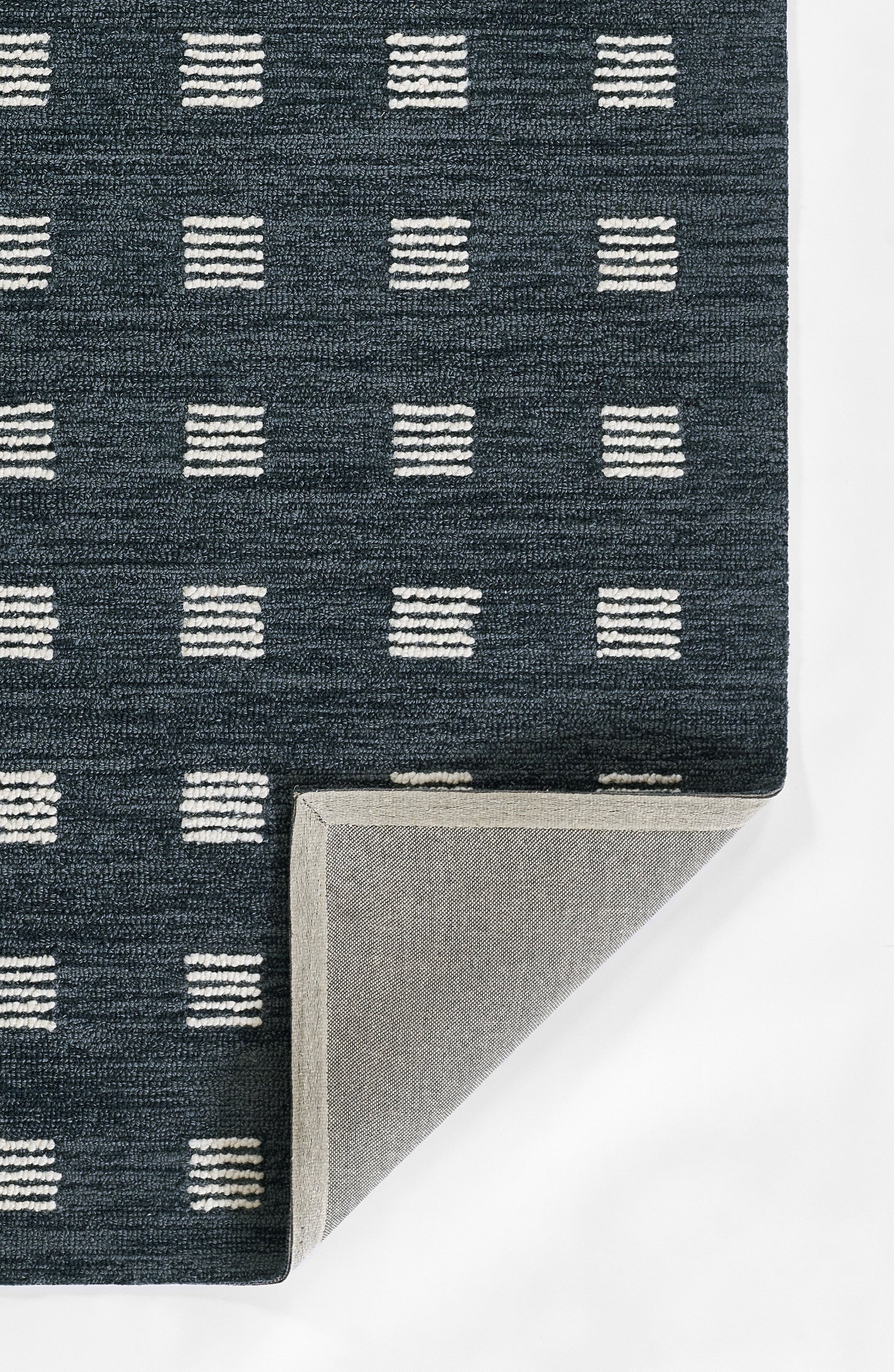 Navy blue woven rug with white stacked-dash square pattern; folded corner reveals light gray underside.