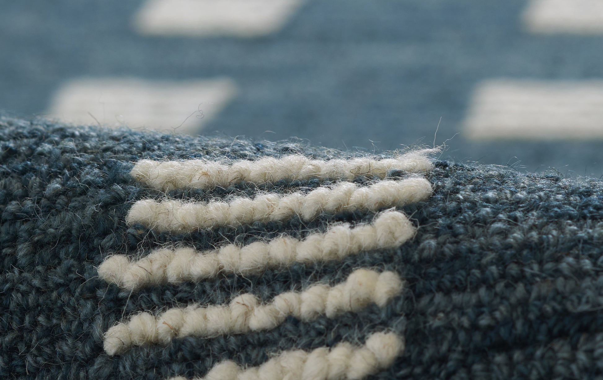 Close-up of dark blue woven rug with cream chunky yarn embroidery forming curved stripes.