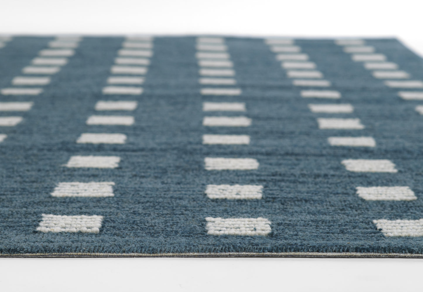 Blue woven area rug with white rectangular dash pattern in vertical rows; low-pile & modern geometric style.