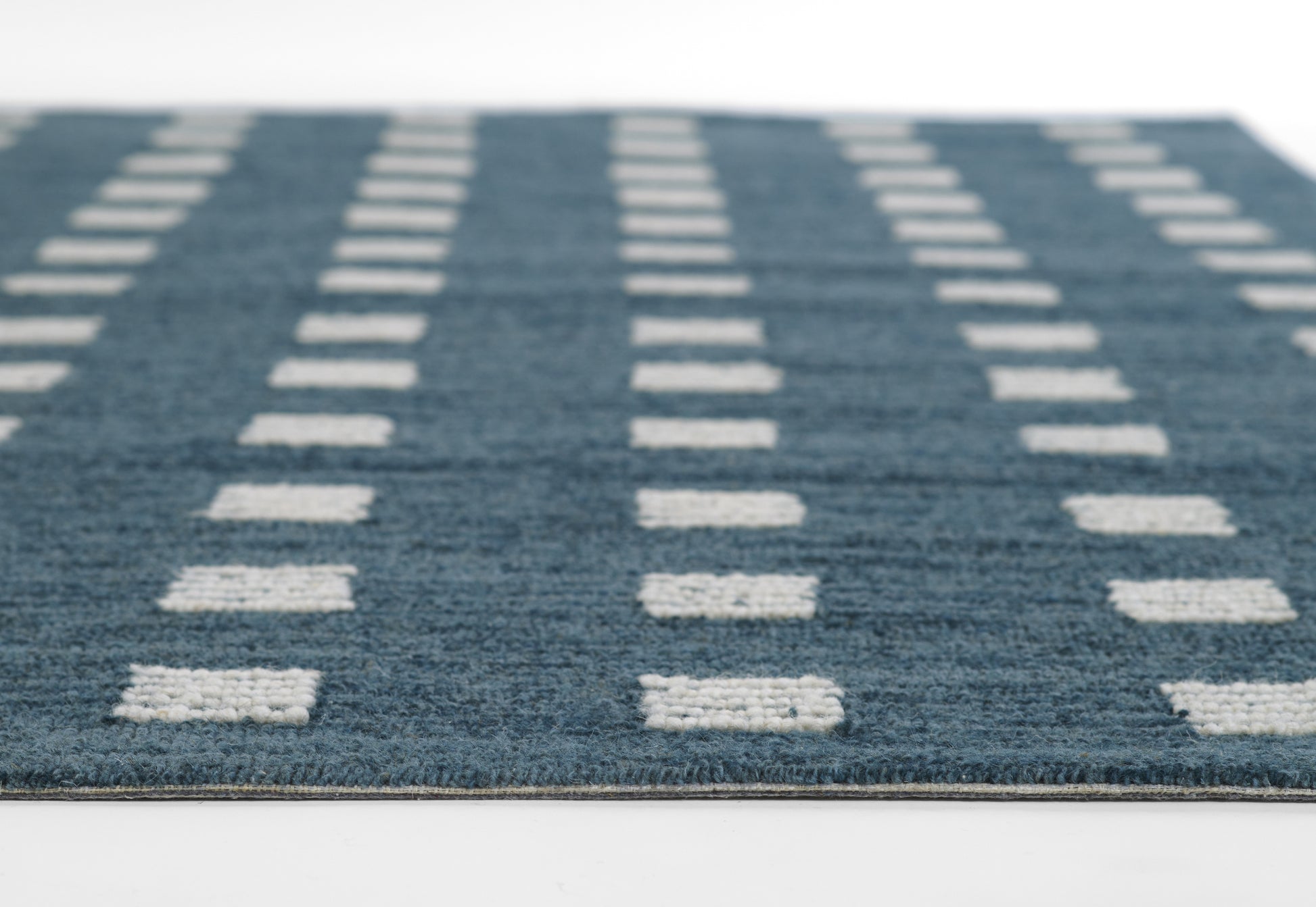 Blue woven area rug with white rectangular dash pattern in vertical rows; low-pile & modern geometric style.
