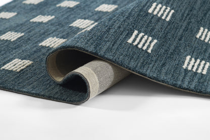 Blue woven rug with white rectangular dash motifs, rolled to reveal beige backing.