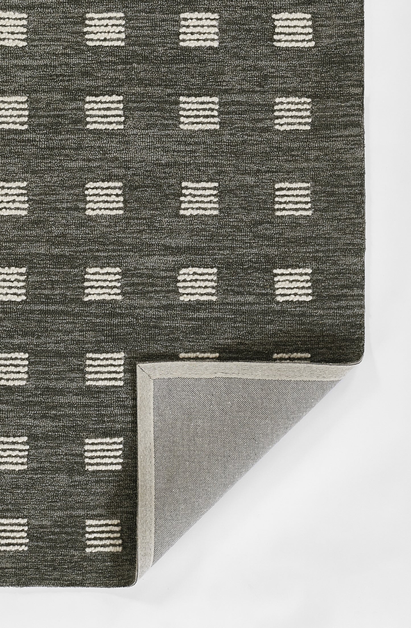 Charcoal woven rug with white dashed-square grid; folded corner reveals light gray underside.