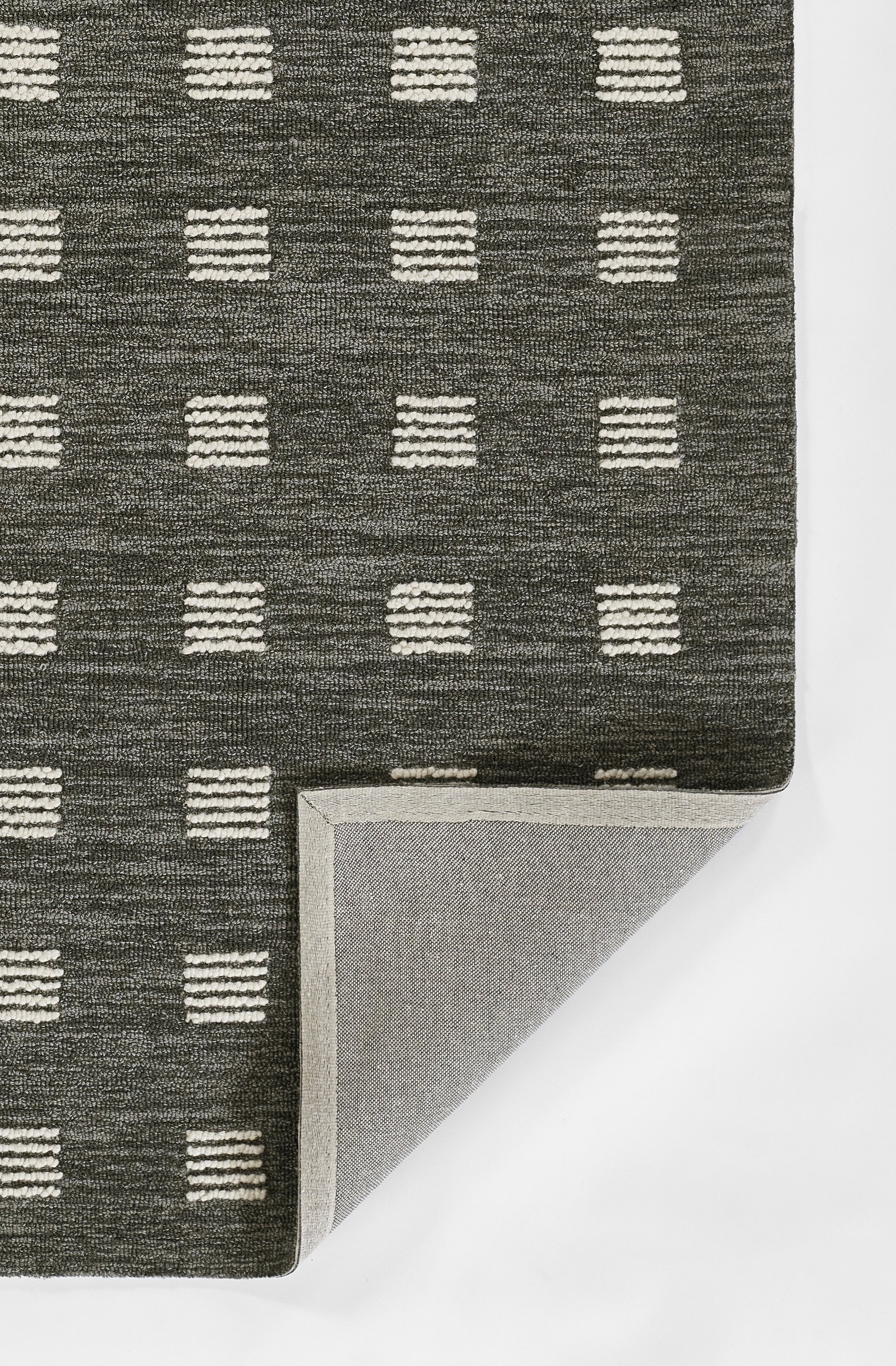 Charcoal low-pile rug with evenly spaced white dashed-square grid; corner folded to reveal light gray underside.