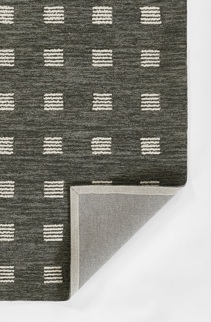 Charcoal low-pile rug with evenly spaced white dashed-square grid; corner folded to reveal light gray underside.