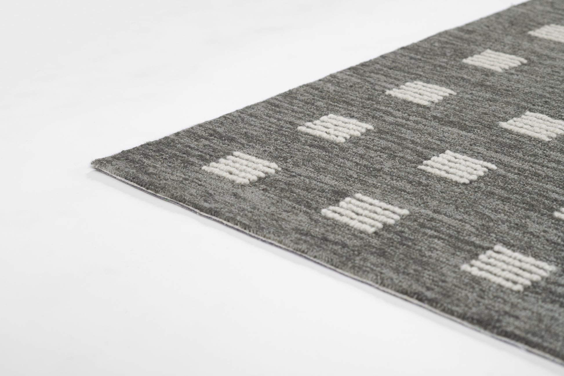Gray tufted rug with white square geometric blocks; modern rectangular floor covering.