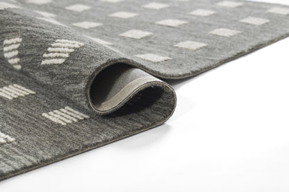 Close-up of gray rug with white diamond pattern, plush pile; rolled edge shows underside.