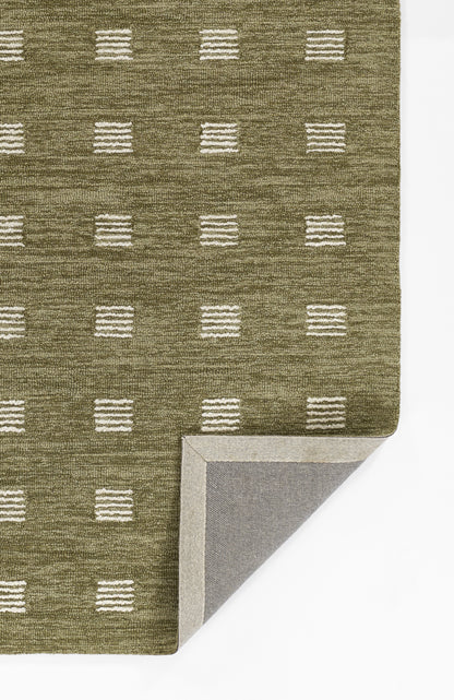 Olive green woven rug with white dashed square pattern; folded corner reveals gray backing, contemporary geometric style.
