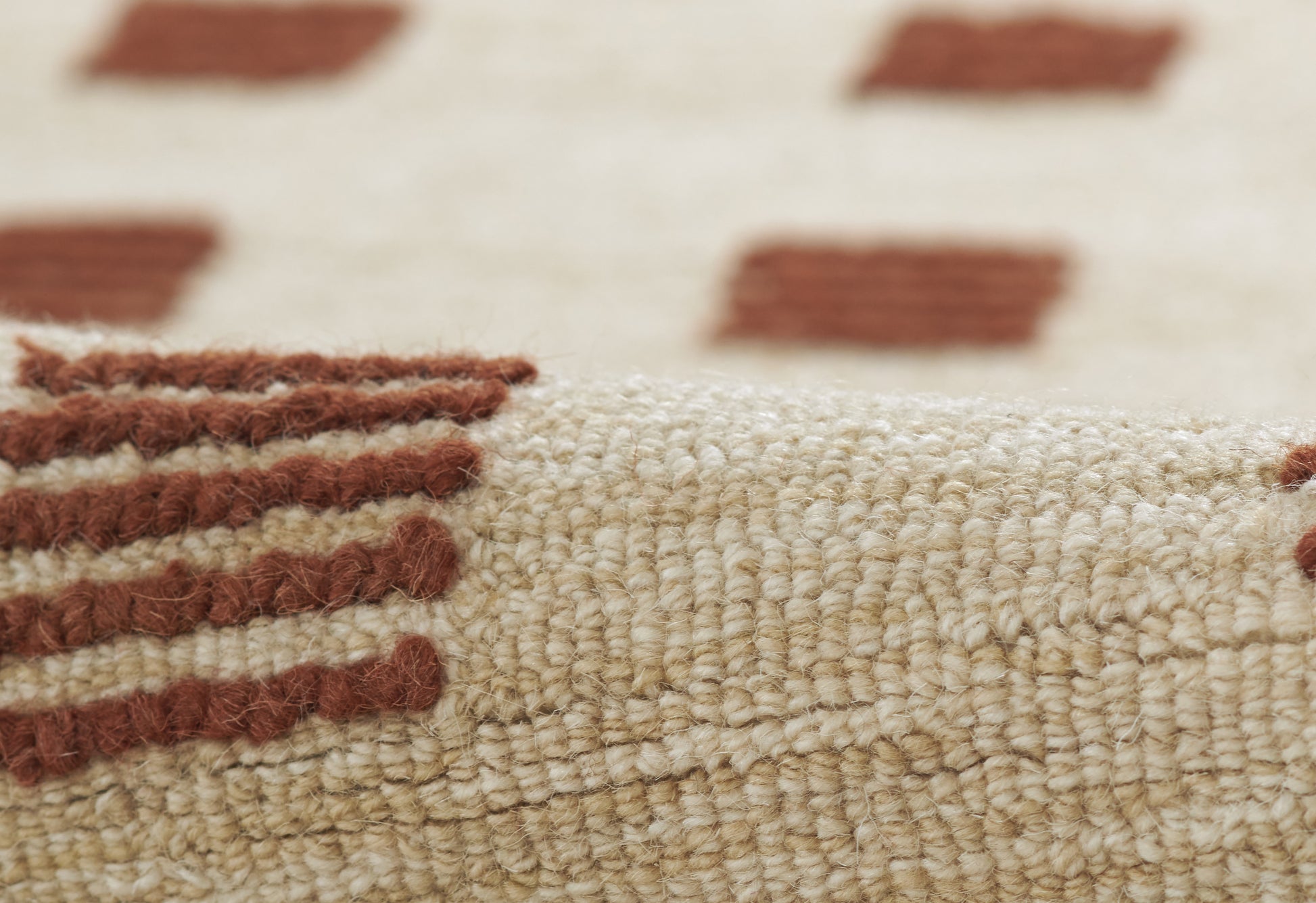 Beige woven rug with rust-brown rectangular motifs; close-up showing thick pile and edge detail.