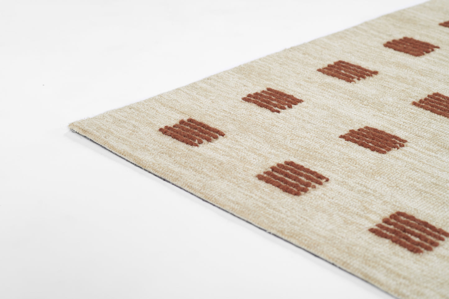 Beige woven rug with rust brown square motifs in a grid, edge view, soft textured area rug for living room decor