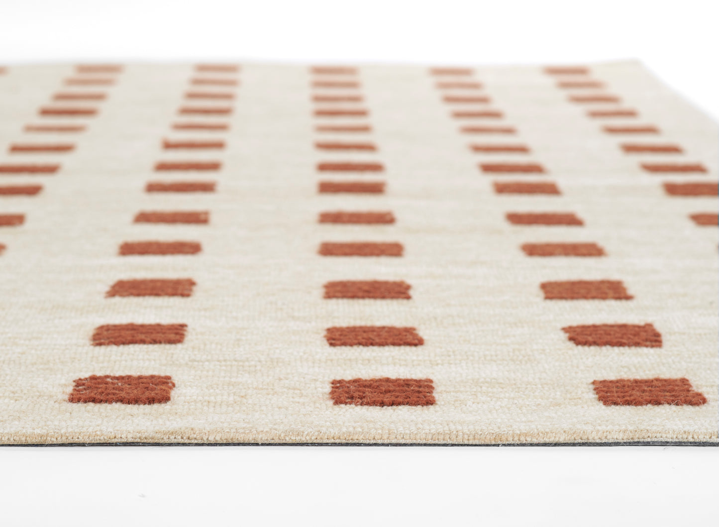 Beige woven rug with rust-orange rectangular blocks in vertical rows, textured surface laid flat on a white studio backdrop.