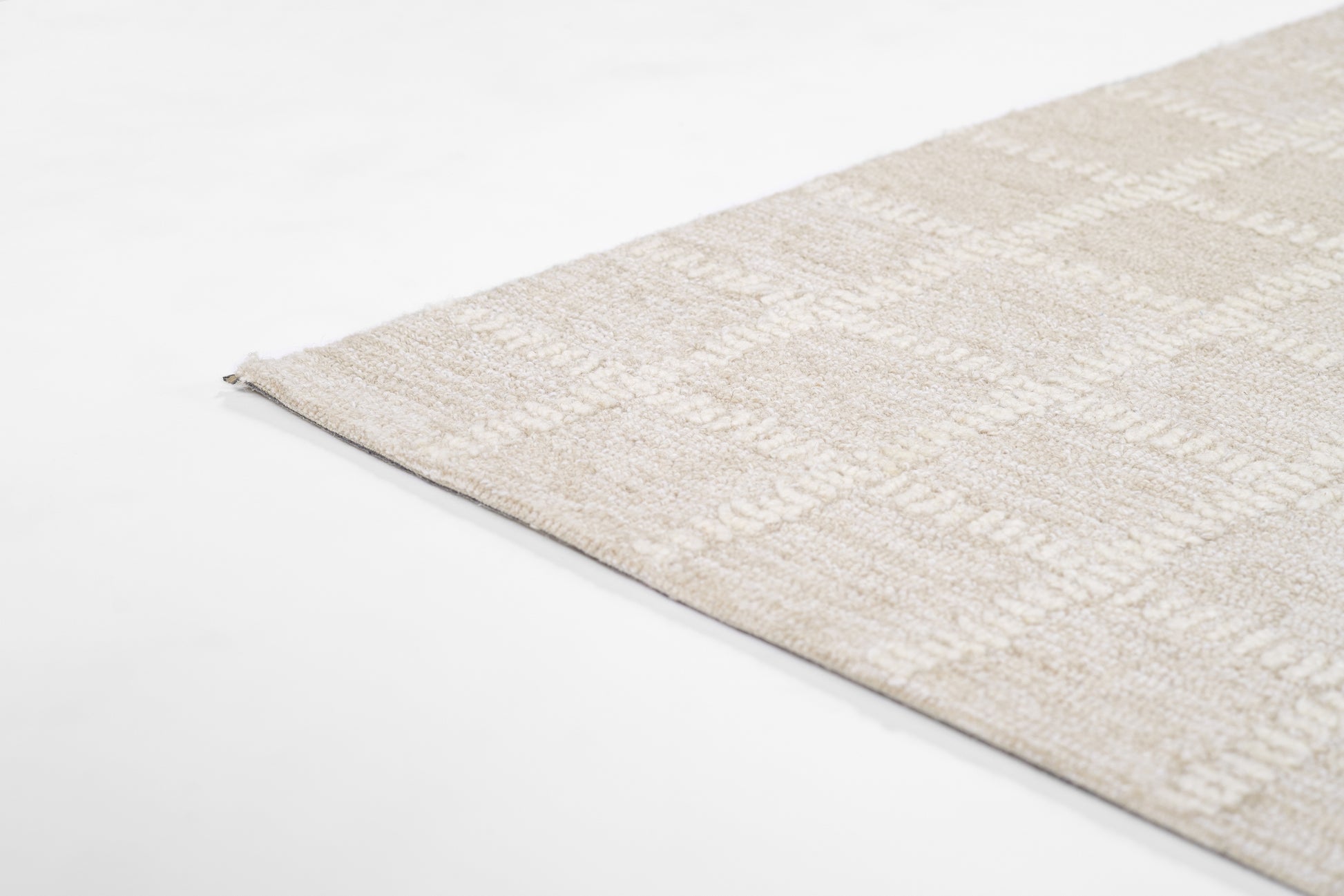 Beige textured area rug with subtle geometric pattern and soft plush pile, corner view.