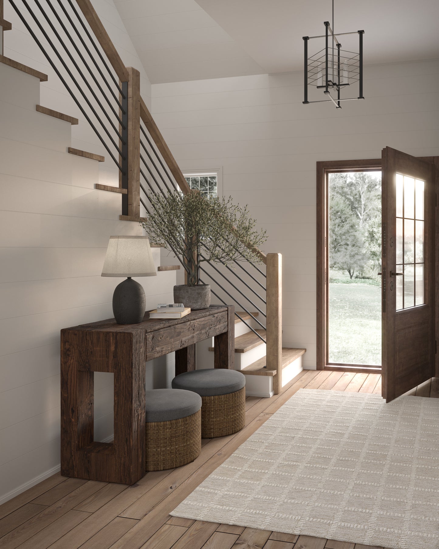 Rustic entryway with dark wood console, wicker ottomans, gray cushions, plant, and stairs with wood treads and black rail.