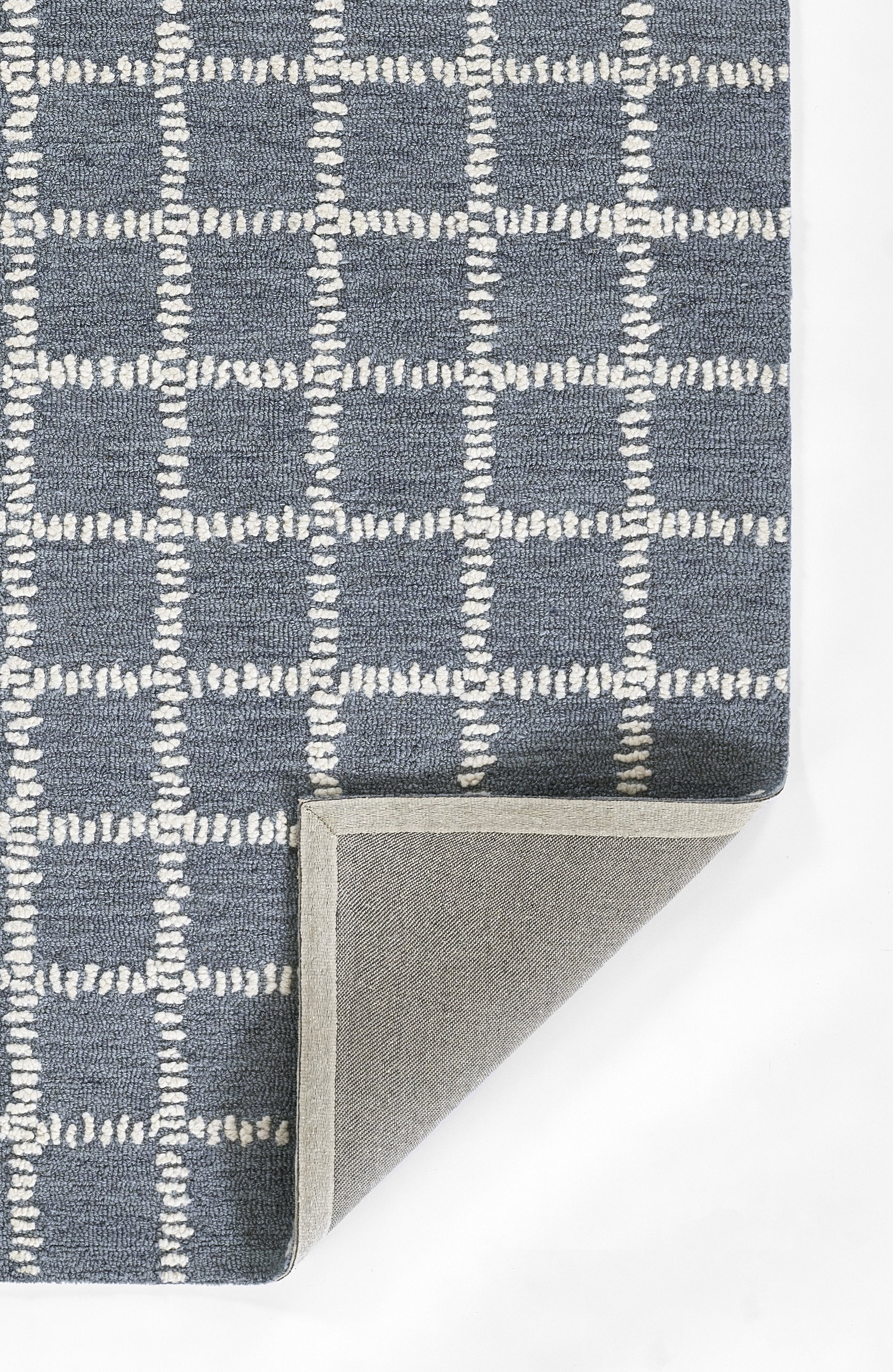 Blue-gray rug with white stitched grid pattern; checkered squares, folded corner shows light gray underside.