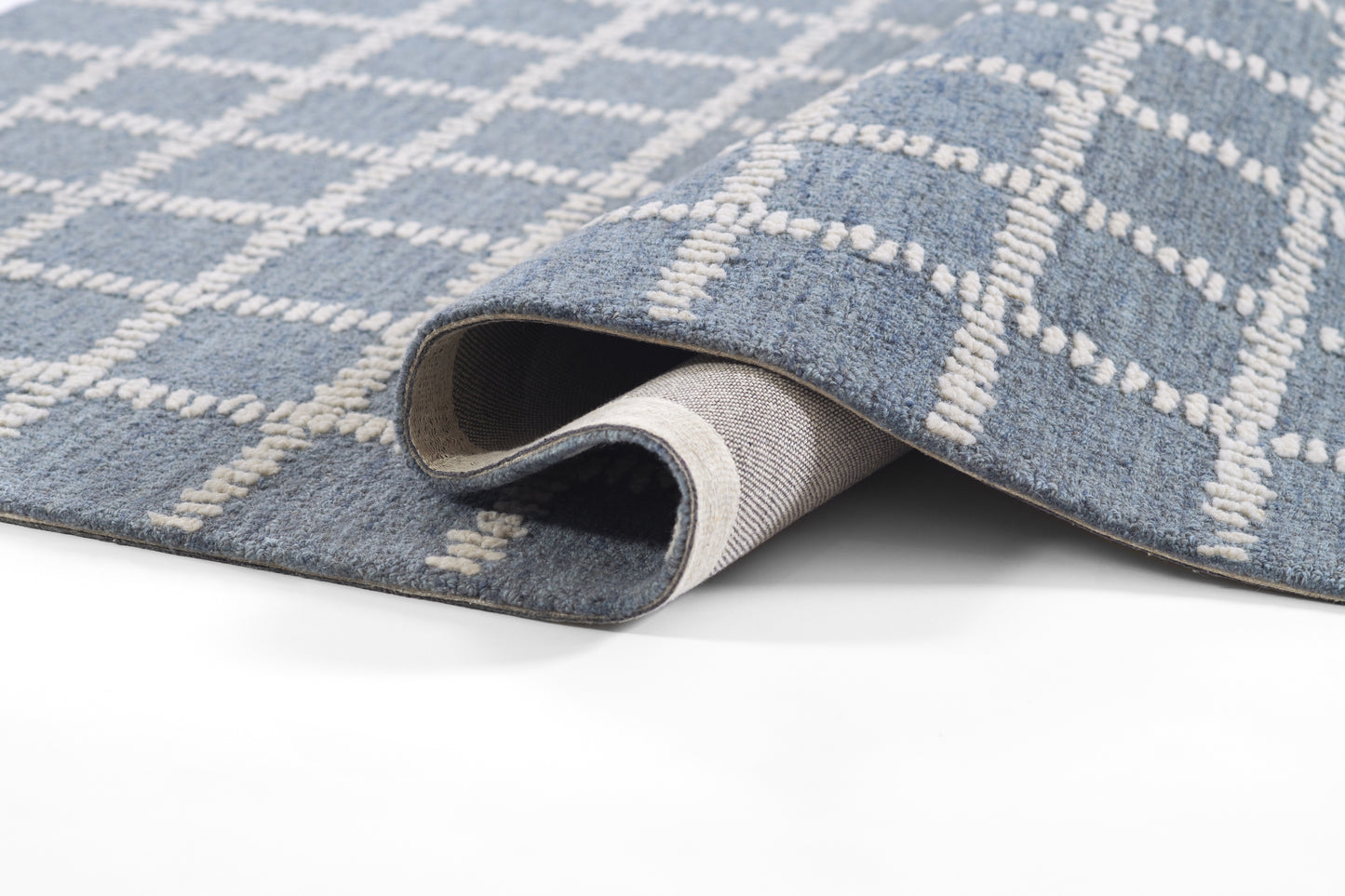Blue woven rug with white geometric lattice pattern, rolled corner reveals soft pile & light gray backing.