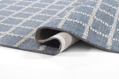 Blue woven rug with white geometric lattice pattern, rolled corner reveals soft pile & light gray backing.