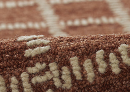 Close-up of a brown tufted rug with cream beige motifs; wool texture and rustic geometric pattern.