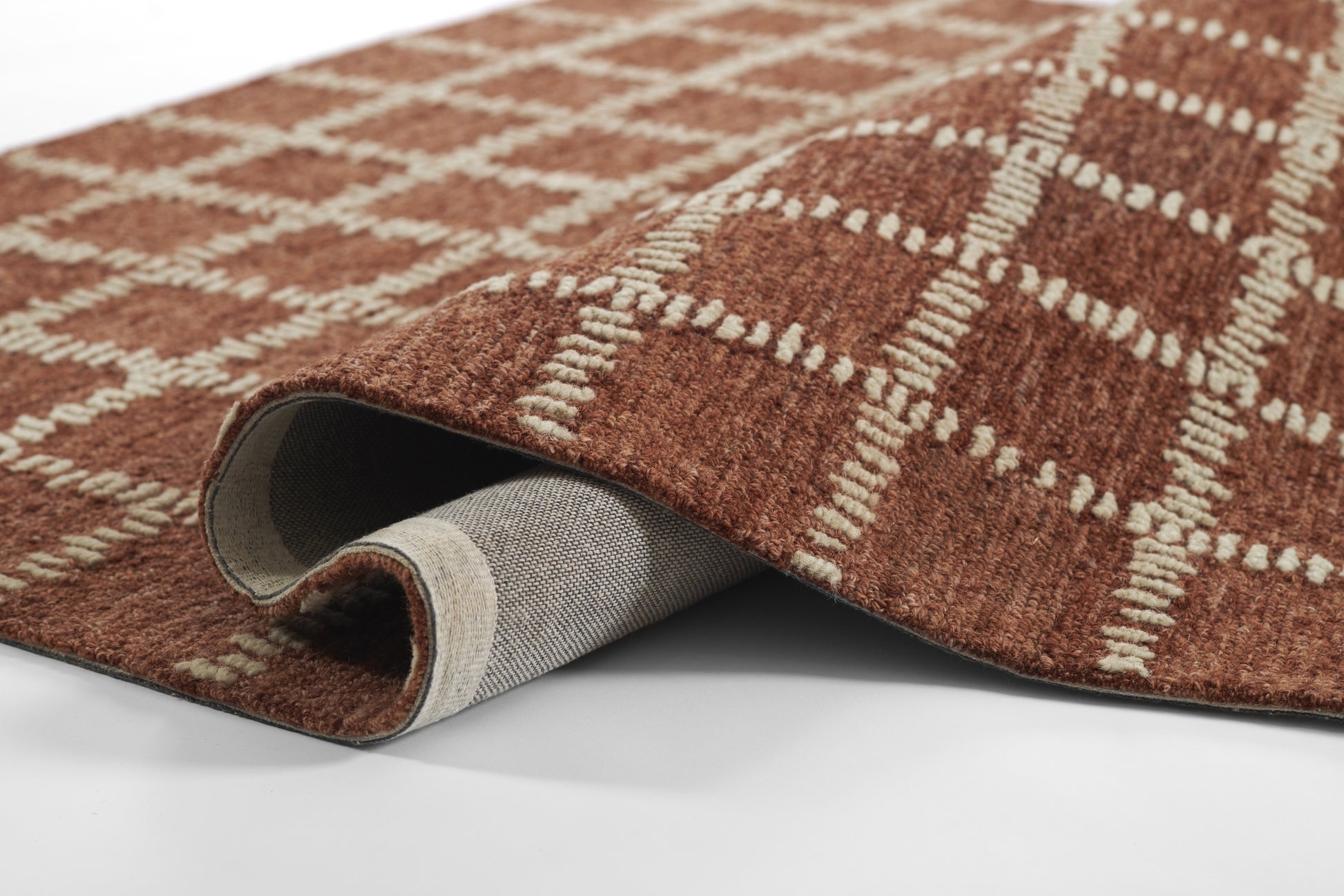 Brown plaid area rug with cream geometric lines, thick woven texture; rolled edge reveals grey underside.