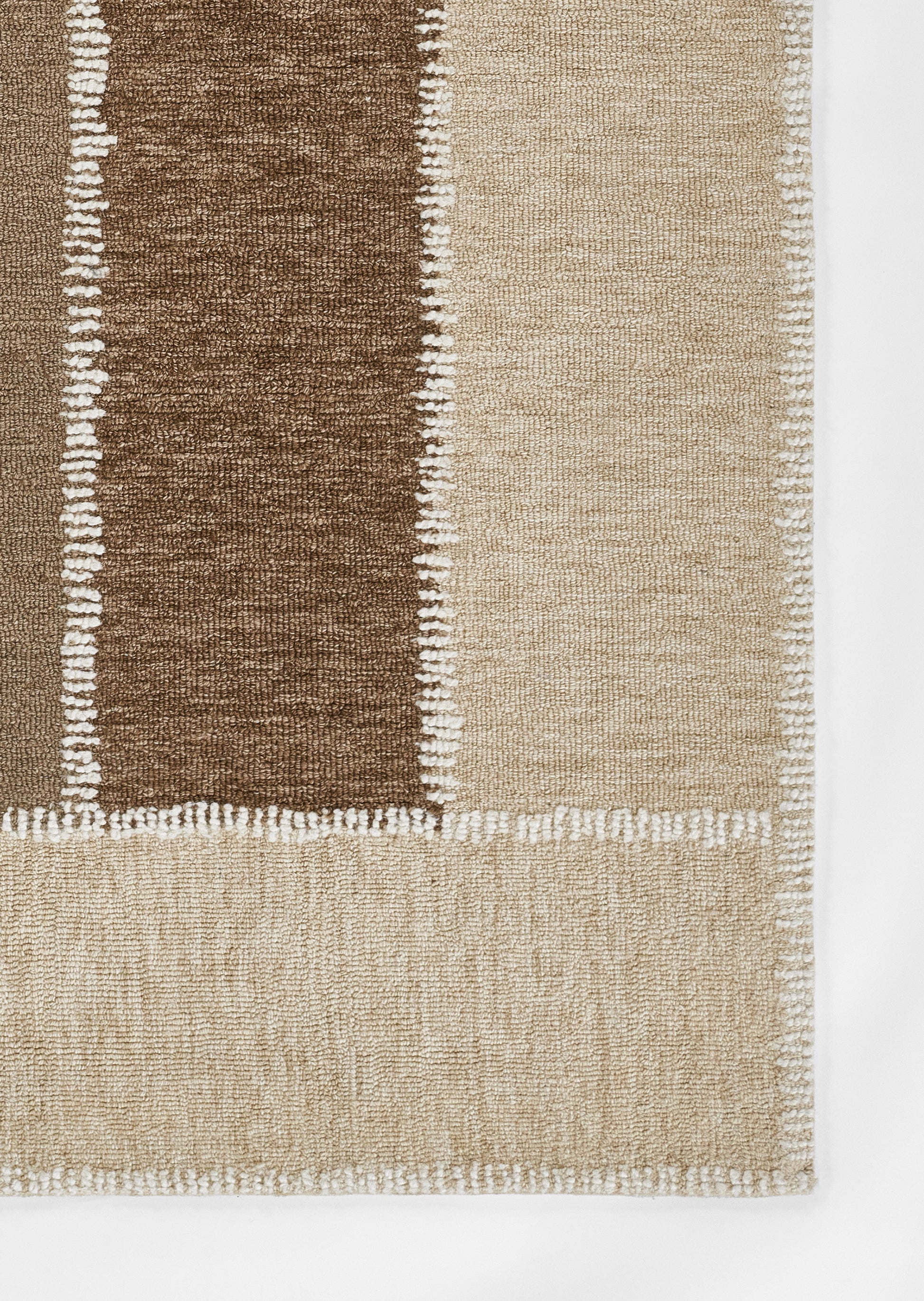 Rectangular woven rug with dark brown and beige blocks, white knotted border, textured surface; modern geometric style.