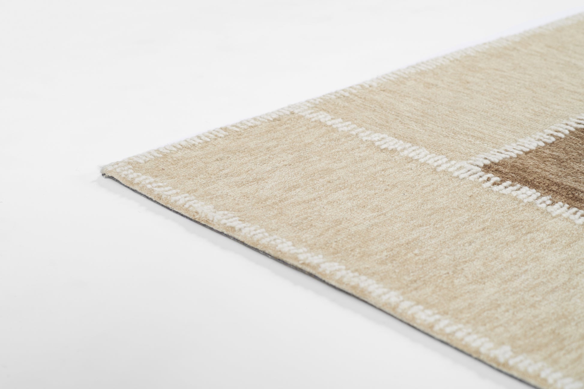 Beige patchwork area rug with cream borders and brown squares; soft, low-pile, contemporary decor.