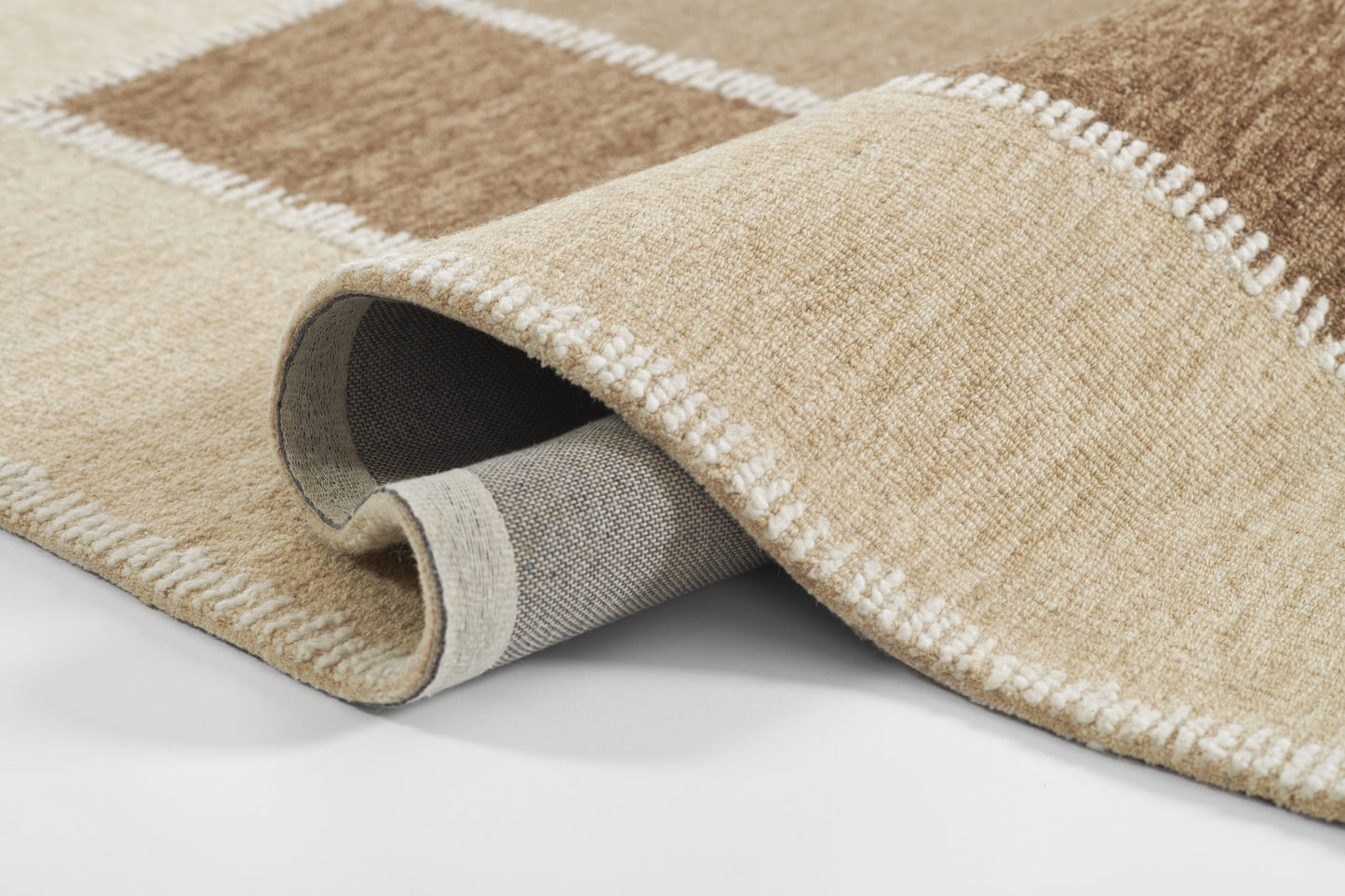 Beige and tan woven area rug with geometric square motif, white border stitching, rolled to reveal gray underside.