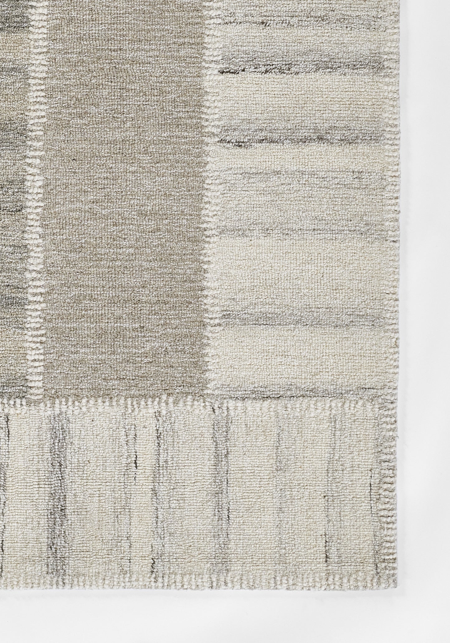 Neutral gray patchwork area rug with woven texture and fringe edge, modern geometric style.