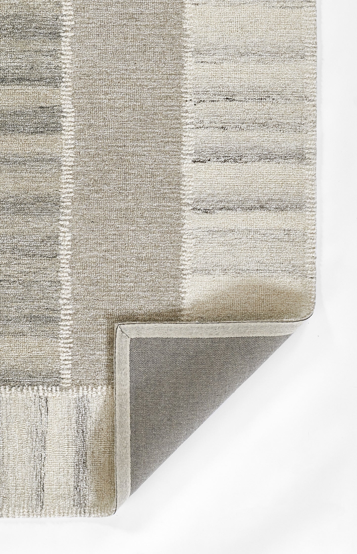 Rectangular neutral patchwork rug in gray and beige tones with tufted pile and folded corner showing non-slip backing.
