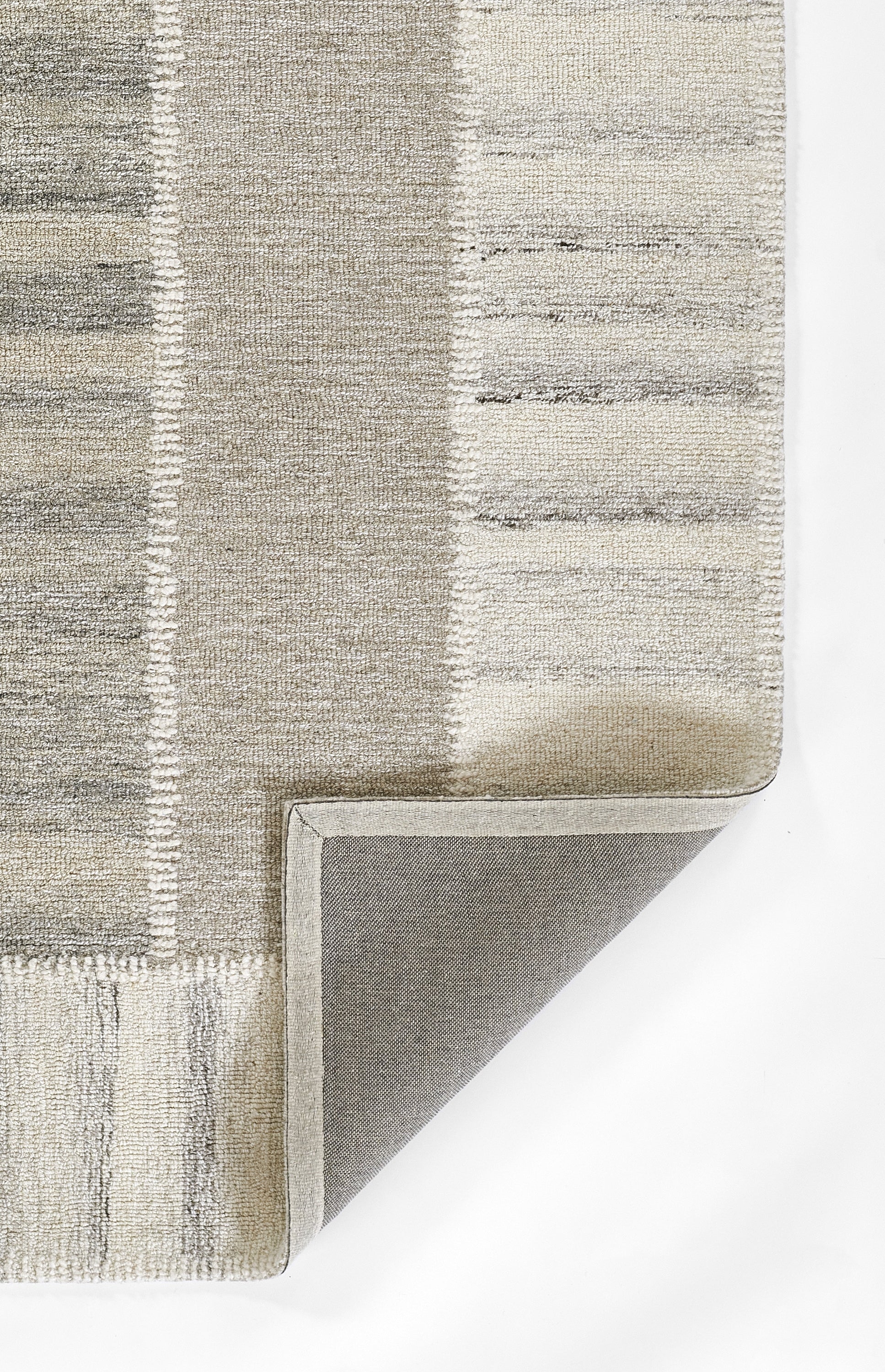 Rectangular neutral patchwork rug in gray and beige tones with tufted pile and folded corner showing non-slip backing.
