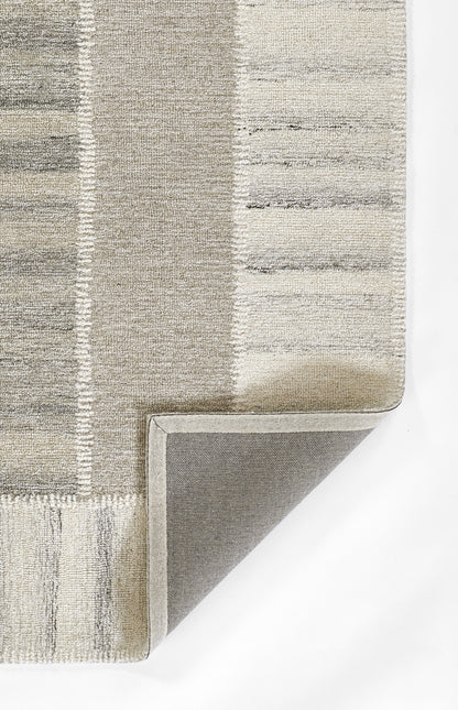 Rectangular neutral patchwork rug in gray and beige tones with tufted pile and folded corner showing non-slip backing.