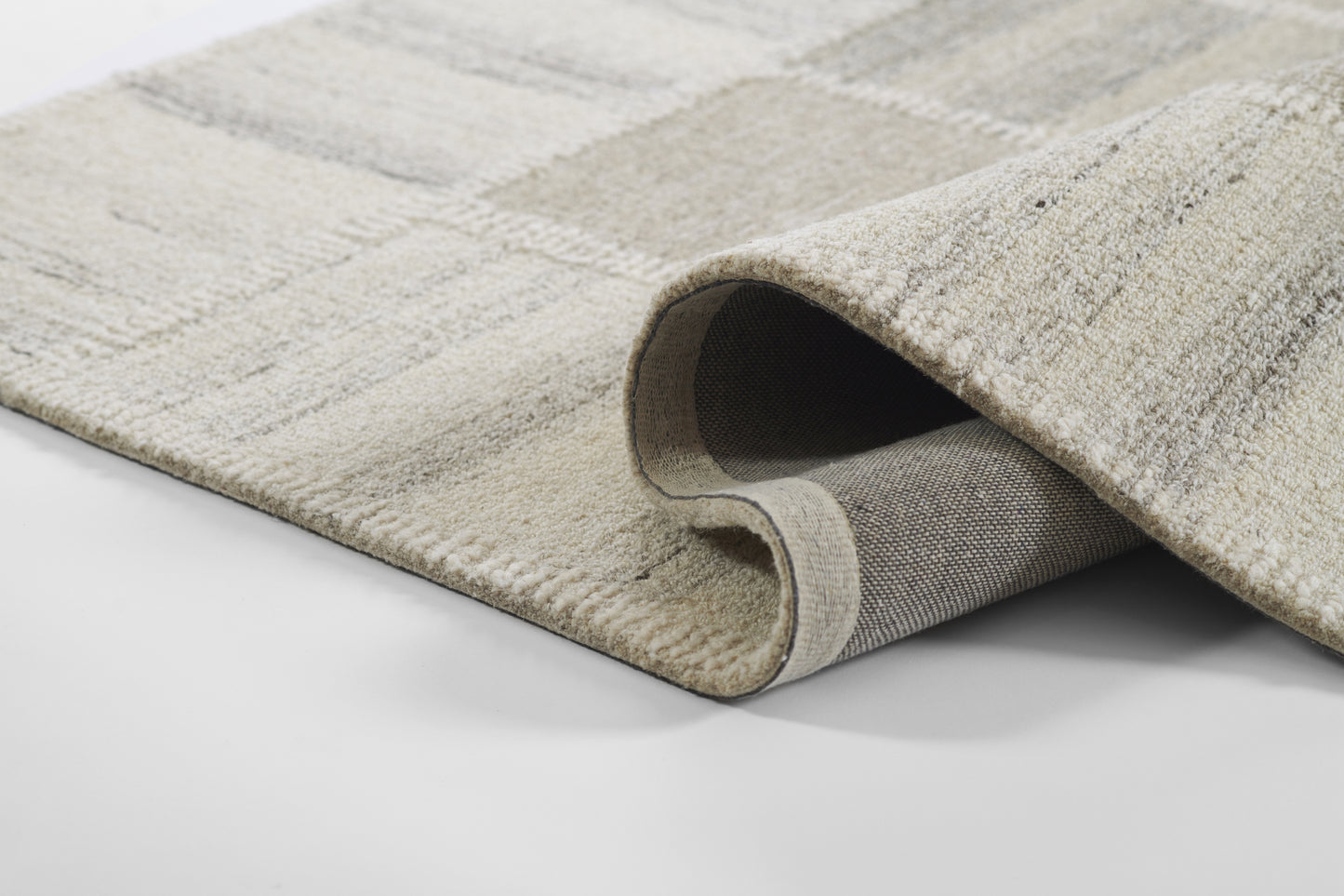 Beige-gray patterned area rug with plush pile; rolled corner reveals gray backing for modern living room decor.