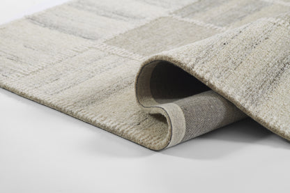 Beige-gray patterned area rug with plush pile; rolled corner reveals gray backing for modern living room decor.