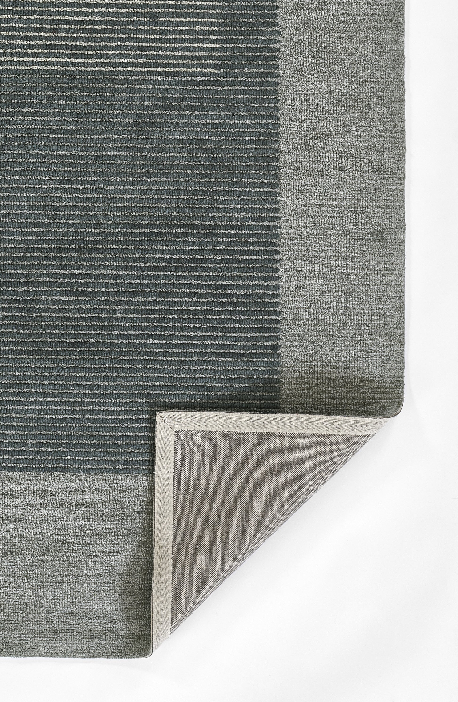 Blue-gray woven area rug with light gray border; textured striped pattern, corner folded to reveal underside.