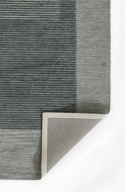 Blue-gray woven area rug with light gray border; textured striped pattern, corner folded to reveal underside.