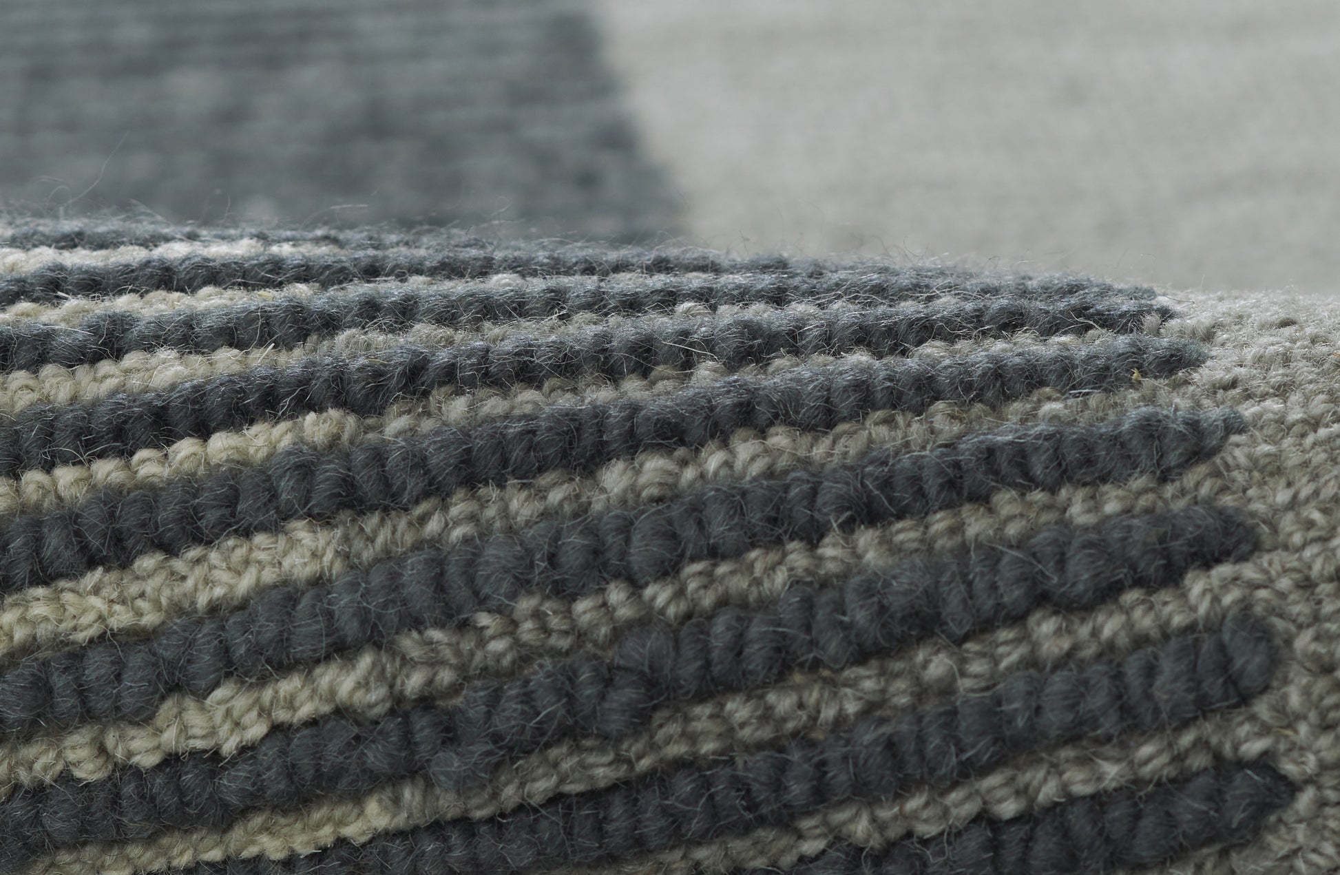 Close-up of a chunky wool striped area rug in navy blue, gray and beige with thick woven pile.