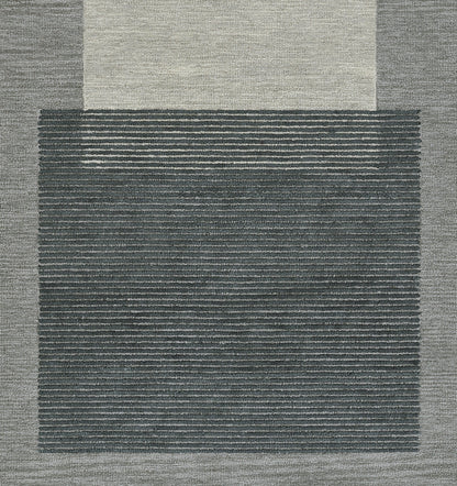 Blue-gray area rug with a dark striped central panel and light beige outer border; modern geometric, textured weave.