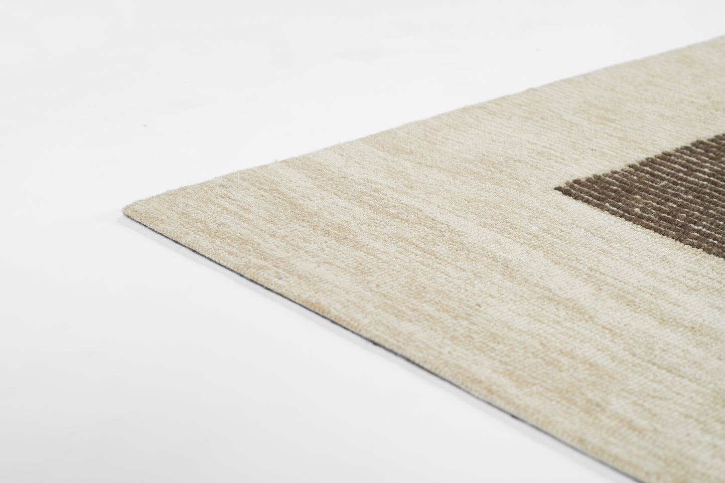 Beige rectangular area rug with a dark brown geometric block, soft textured pile, ideal for living room decor.