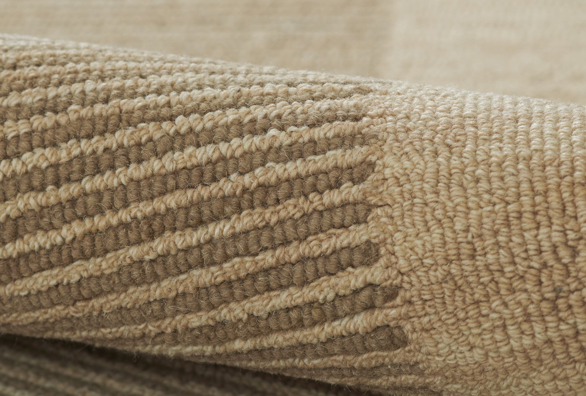 Rolled edge of beige-tan textured rug with striped pattern; thick woven loop pile for cozy home decor.