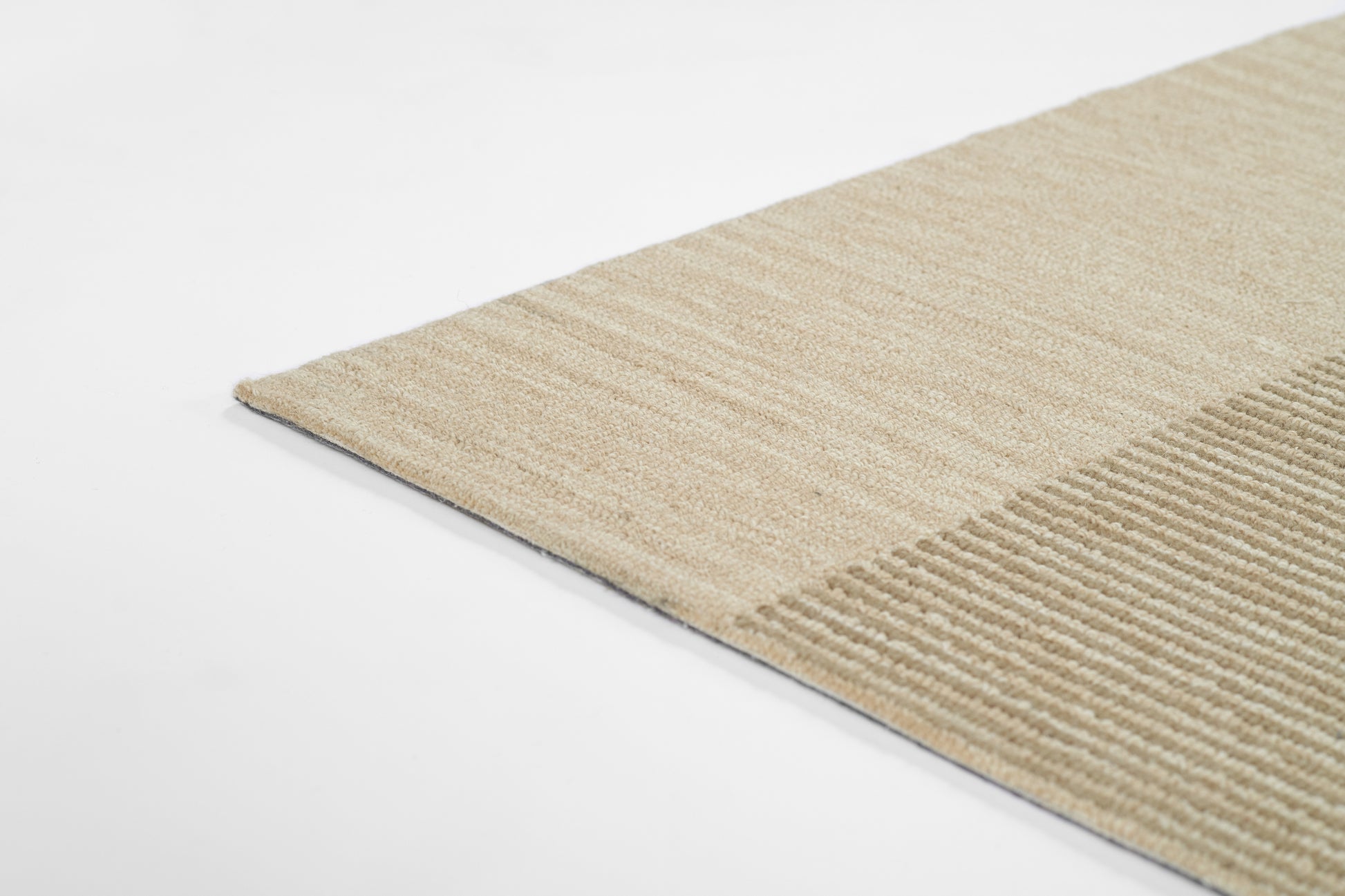 Beige area rug corner with smooth woven section and ribbed stripe; neutral, modern home decor.