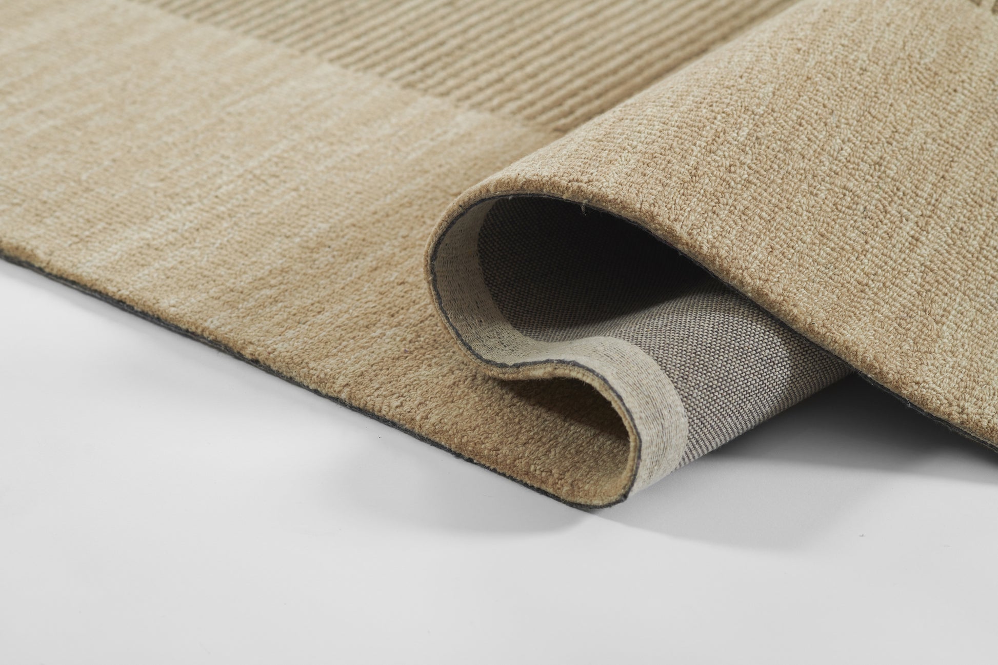 Beige high-pile area rug, curled corner exposing gray backing and woven underside.