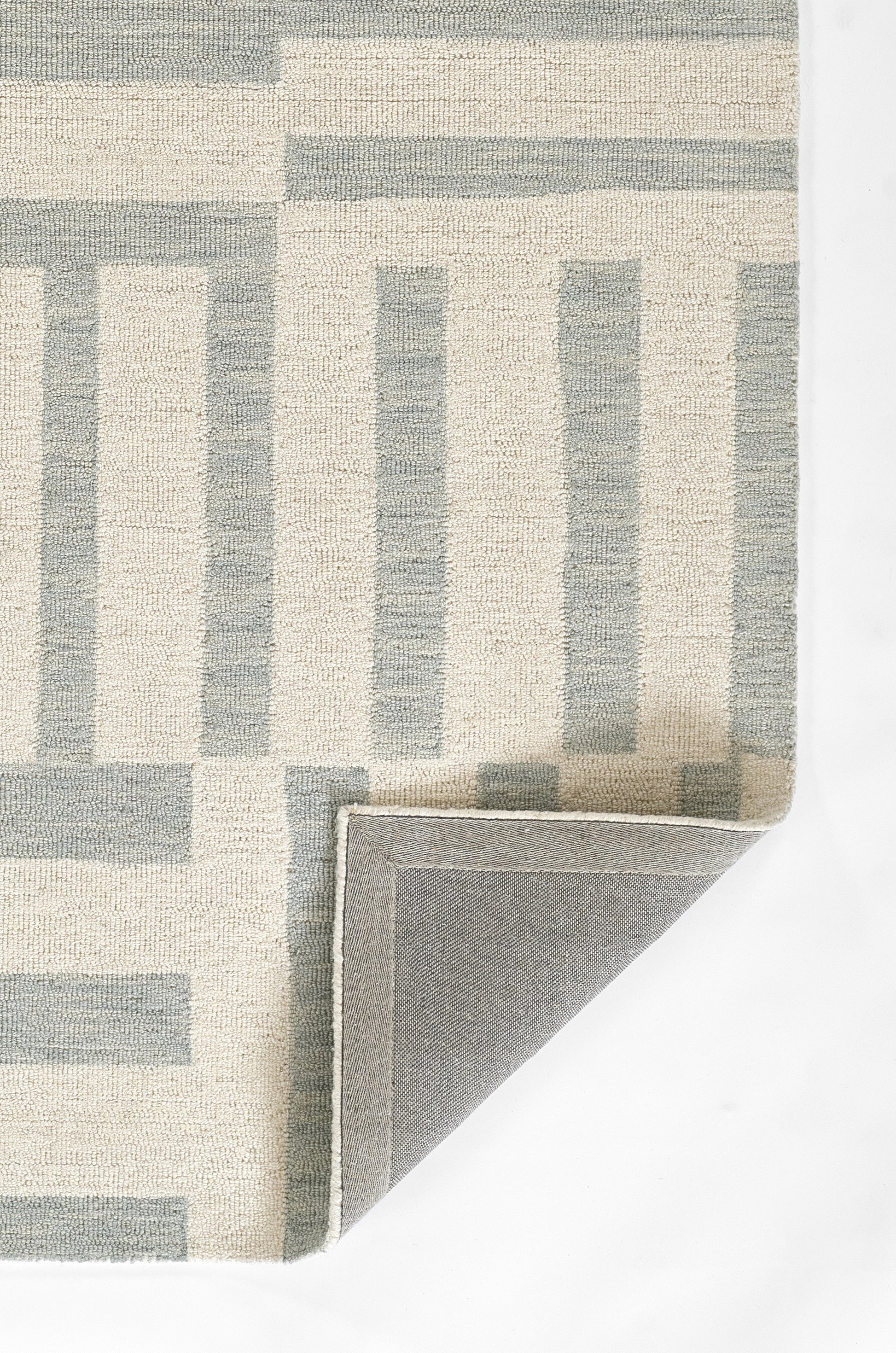 Beige geometric rug with blue-gray rectangular borders; woven texture, corner folded to reveal gray underside.