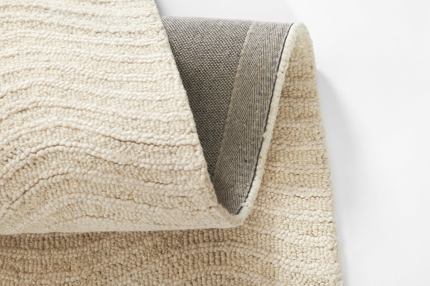 Cream boucle shag rug with plush textured pile; rolled edge reveals gray woven backing.